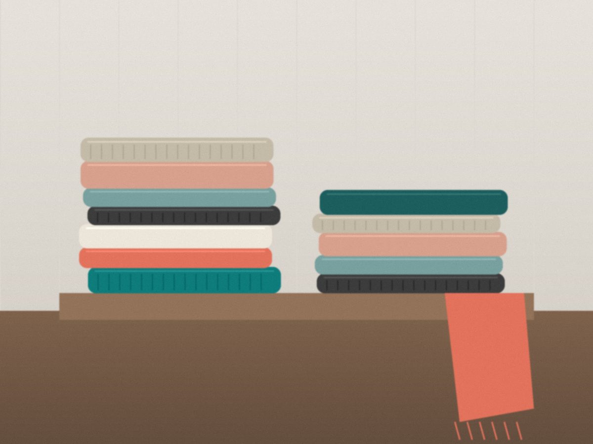 Folded linen and wool throws in teal, coral and natural tones stacked on a wooden bench